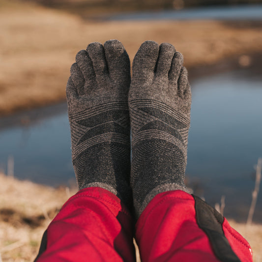 Person wearing gray toe-separated socks with red pants by a body of water.